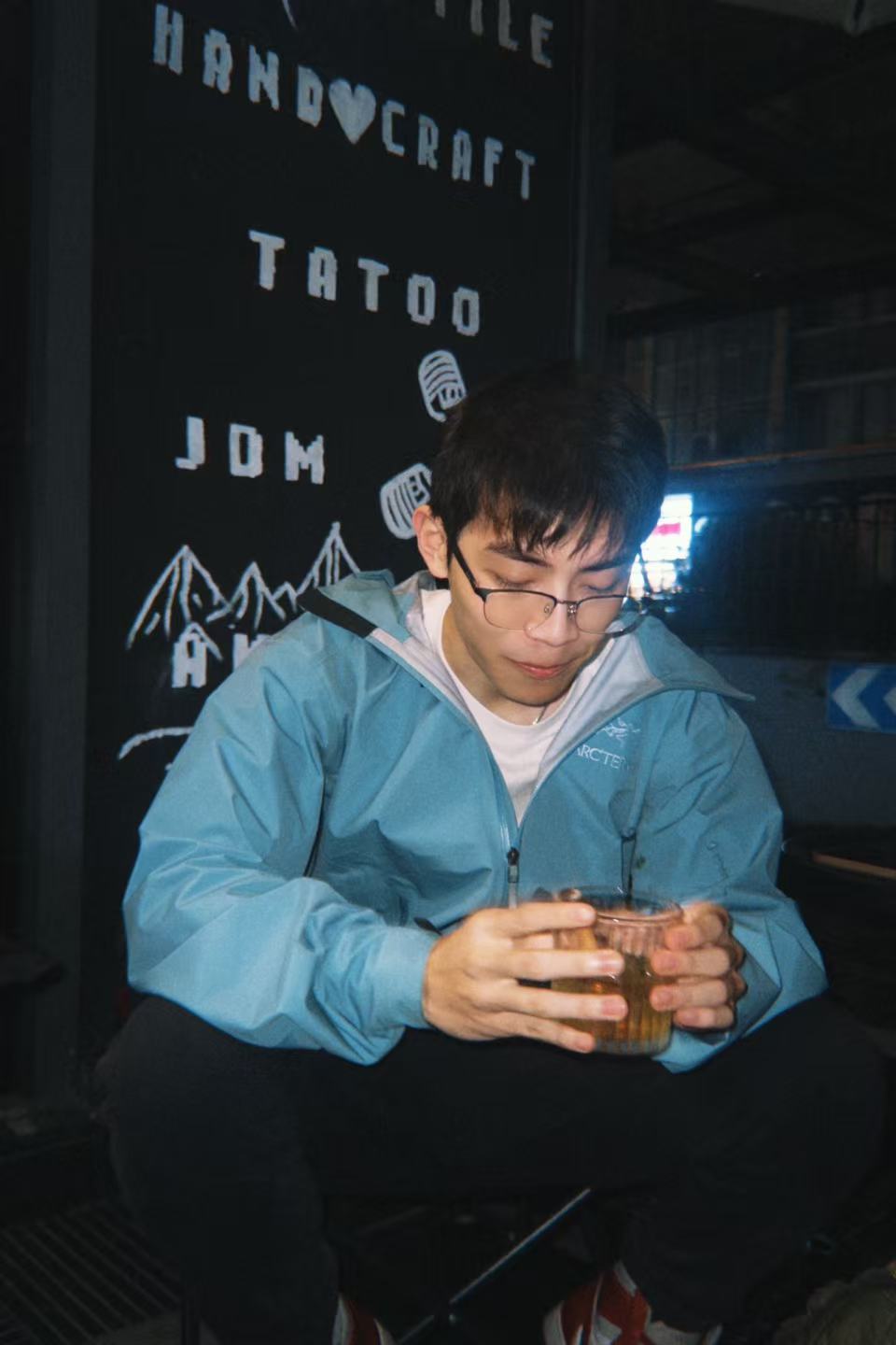 A person in a blue jacket holding a drink at night